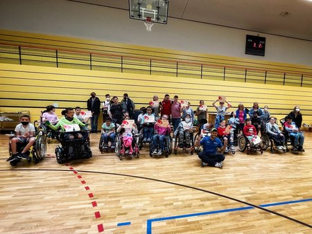 Circa 20 Teilnehmende im Rollstuhl und zu Fuß in einer Sporthalle.