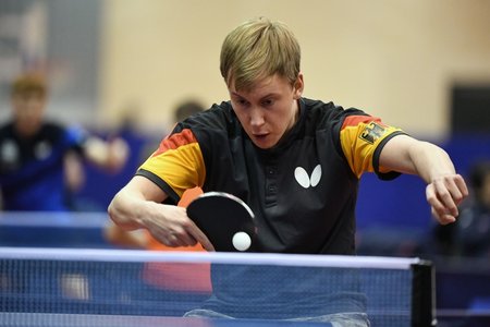 Ein junger Tischtennisspieler im schwarzen Deutschlandtrikot schlägt den Ball mit der Rückhand.