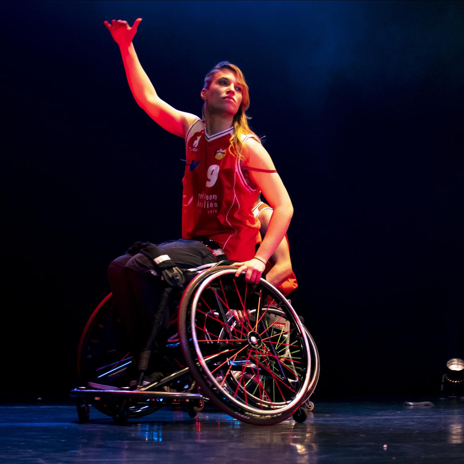 Rollstuhlbasketballerin im roten Trikot in Nahaufnahme hebt den rechten Arm.