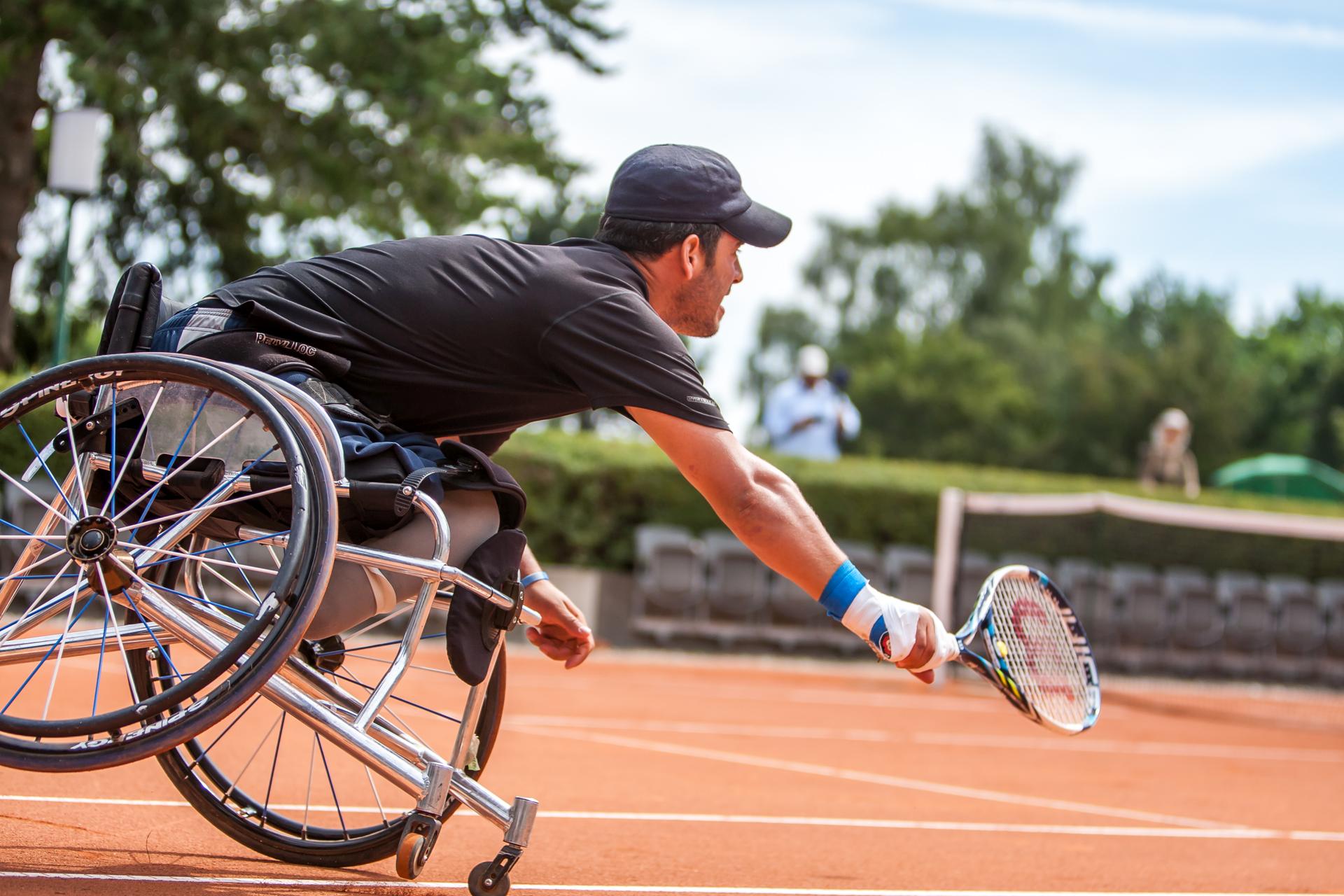 Rollstuhl-Tennisspieler kippt leicht nach vorne mit ausgestrecktem Schläger.