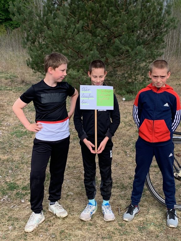 Drei stehende Jungs in Sportsachen. Der mittlere hält ein Schild mit der Aufschrift: "Wir laufen für den 1. Berliner Inklusions-Tauchclub." 